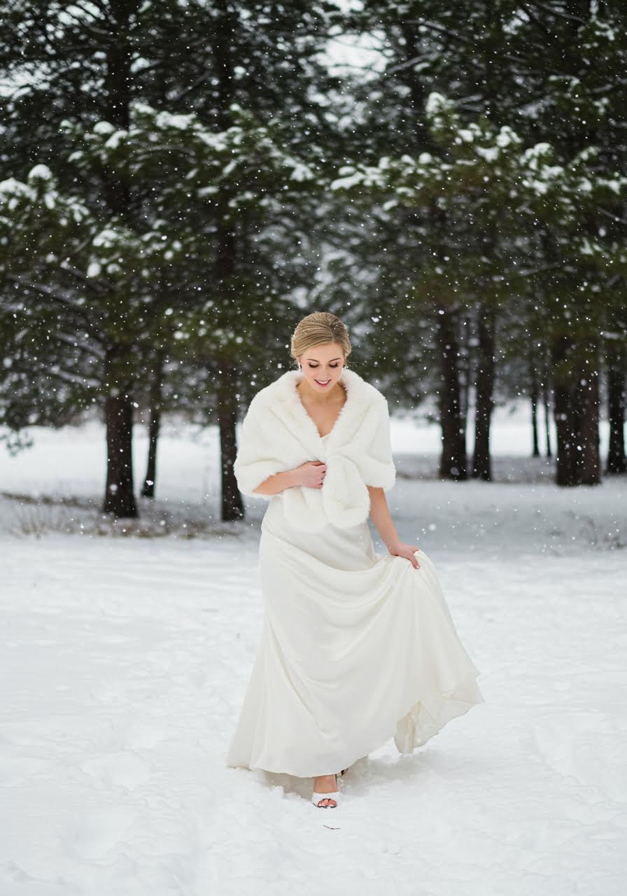 Bride wearing ivory faux fur stole with wedding dress among snow-covered pine trees